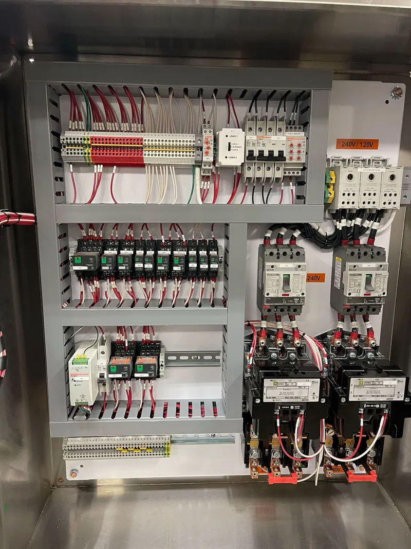 A stainless steel control panel for two motors, door open: two starters and two breakers on the right; relays, terminal blocks and an alternating relay on the left